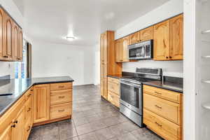 Kitchen featuring kitchen peninsula, light brown cabinets, stainless steel appliances, dark stone countertops, and tile patterned flooring