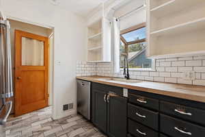 Kitchen featuring stainless steel dishwasher, butcher block counters, sink, and backsplash