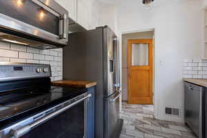 Kitchen with butcher block countertops, backsplash, stainless steel appliances, and white cabinets