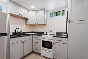 Kitchen featuring a textured ceiling, stainless steel fridge, white gas stove, sink, and light wood-type flooring