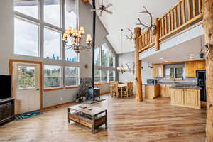 Living room featuring ceiling fan with notable chandelier, high vaulted ceiling, a wood stove, and light hardwood / wood-style floors