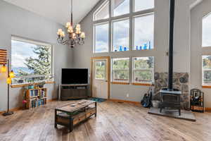 Living room featuring high vaulted ceiling, a wood stove, an inviting chandelier, and light hardwood / wood-style flooring