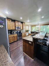 Kitchen featuring stainless steel appliances, dark hardwood / wood-style flooring, an island with sink, light stone countertops, and sink