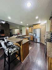 Kitchen with a kitchen island with sink, tasteful backsplash, a kitchen bar, dark wood-type flooring, and appliances with stainless steel finishes