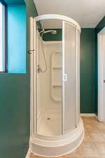 Bathroom featuring tile patterned floors, walk in shower, and a textured ceiling