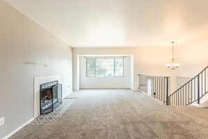 Unfurnished living room featuring carpet flooring, a tiled fireplace, and a notable chandelier