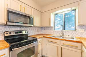 Kitchen with sink, appliances with stainless steel finishes, white cabinets, and tasteful backsplash