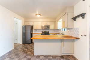 Kitchen featuring backsplash, appliances with stainless steel finishes, sink, butcher block countertops, and a kitchen breakfast bar