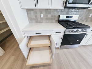 Kitchen featuring backsplash, stainless steel appliances, white cabinetry, light stone counters, and light wood-type flooring