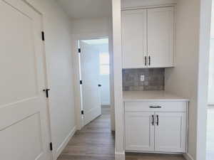 Bar featuring light wood-type flooring, light stone counters, backsplash, and white cabinetry