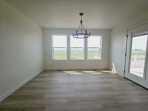 Unfurnished dining area featuring a wealth of natural light, a chandelier, a textured ceiling, and light hardwood / wood-style flooring