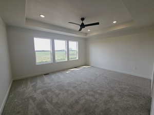 Empty room with a raised ceiling, a textured ceiling, ceiling fan, and carpet