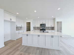 Kitchen featuring a center island with sink, light hardwood / wood-style flooring, appliances with stainless steel finishes, sink, and white cabinetry