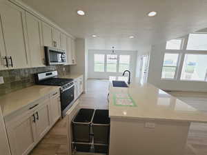 Kitchen featuring appliances with stainless steel finishes, light stone counters, a center island with sink, and sink