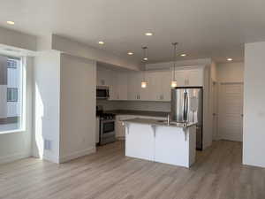 Kitchen featuring stainless steel appliances, shaker cabinetry, hanging light fixtures, island with sink, and laminate wood-style flooring