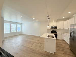 Island kitchen with SS appliances, white shaker cabinetry, pendant light fixtures, open layout, 9' ceilings with light wood floors