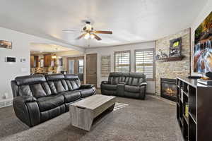 Living room with a textured ceiling, carpet flooring, ceiling fan, and a stone fireplace