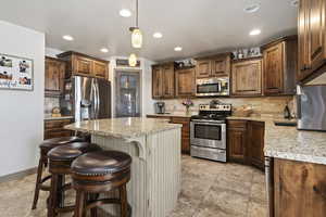 Kitchen with stainless steel appliances, decorative light fixtures, tasteful backsplash, light tile patterned floors, and a kitchen island