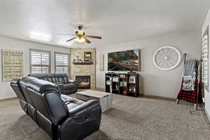 Living room with a fireplace, carpet flooring, ceiling fan, and a textured ceiling