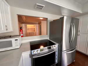 Kitchen with appliances with stainless steel finishes, dark hardwood / wood-style flooring, and white cabinets