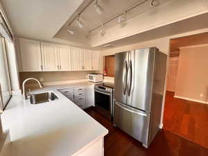 Kitchen featuring rail lighting, stainless steel appliances, sink, dark wood-type flooring, and white cabinets