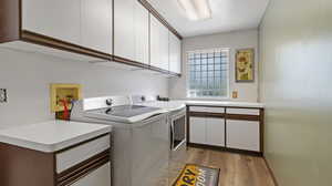 Laundry room with light hardwood / wood-style floors, cabinets, and washing machine and dryer