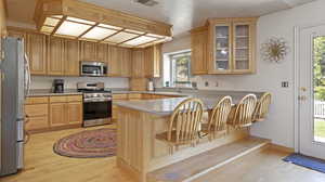 Kitchen featuring a textured ceiling, light hardwood / wood-style flooring, a breakfast bar, kitchen peninsula, and stainless steel appliances