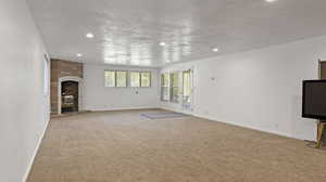 Unfurnished living room featuring light colored carpet, a fireplace, and a textured ceiling