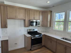 Kitchen with a textured ceiling, light hardwood / wood-style flooring, stainless steel appliances, and tasteful backsplash