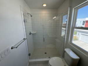 Bathroom featuring a textured ceiling, a healthy amount of sunlight, toilet, and a shower with shower door