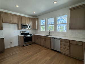 Kitchen with a textured ceiling, light hardwood / wood-style flooring, stainless steel appliances, sink, and decorative backsplash