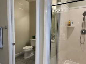 Bathroom featuring toilet, a shower with shower door, and tile patterned floors