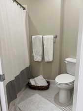 Bathroom with curtained shower, tile patterned flooring, and toilet