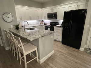 Kitchen featuring black and stianless appliances, kitchen peninsula, sink, and white cabinetry