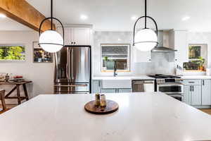 Kitchen with wall chimney exhaust hood, appliances with stainless steel finishes, decorative backsplash, and pendant lighting