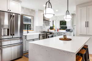 Kitchen with pendant lighting, tasteful backsplash, sink, appliances with stainless steel finishes, and light hardwood / wood-style floors