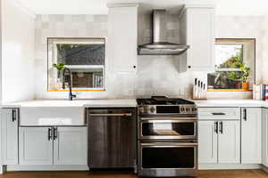 Kitchen with appliances with stainless steel finishes, dark hardwood / wood-style floors, wall chimney exhaust hood, and a healthy amount of sunlight