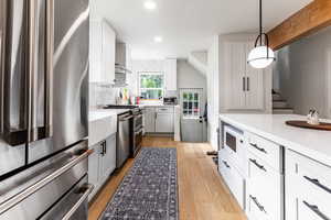 Kitchen featuring pendant lighting, tasteful backsplash, stainless steel appliances, light stone counters, and light wood-type flooring