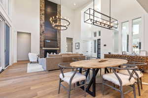 Dining room with light hardwood / wood-style flooring, a fireplace, a notable chandelier, and a towering ceiling