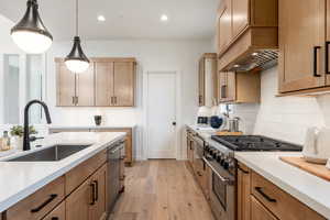 Kitchen featuring custom range hood, light hardwood / wood-style floors, stainless steel appliances, decorative light fixtures, and sink