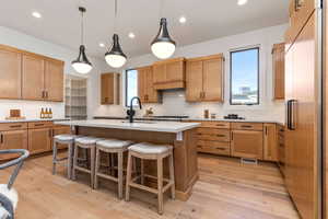 Kitchen with light hardwood / wood-style flooring, a kitchen breakfast bar, stainless steel built in fridge, and a kitchen island with sink