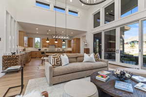 Living room with a towering ceiling, an inviting chandelier, sink, and light hardwood / wood-style floors