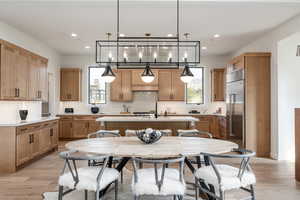 Kitchen featuring stainless steel appliances, a center island with sink, hanging light fixtures, and light wood-type flooring