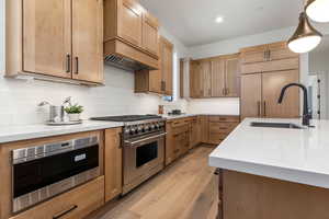 Kitchen featuring light wood-type flooring, sink, decorative backsplash, hanging light fixtures, and appliances with stainless steel finishes