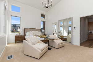 Bedroom featuring multiple windows, high vaulted ceiling, a chandelier, and light colored carpet