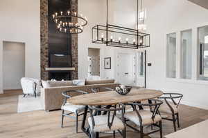 Dining area featuring high vaulted ceiling, light wood-type flooring, an inviting chandelier, and a fireplace