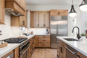 Kitchen with pendant lighting, premium range hood, sink, high end appliances, and light hardwood / wood-style flooring