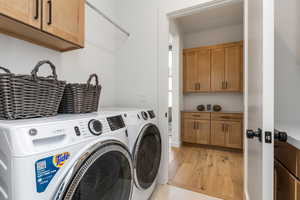 Laundry area with washer and dryer, cabinets, and light wood-type flooring