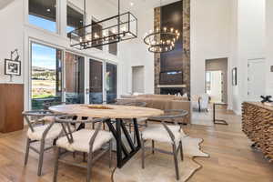 Dining room with a high ceiling, a stone fireplace, a notable chandelier, and light hardwood / wood-style flooring