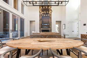 Dining area featuring a high ceiling, a stone fireplace, wood-type flooring, and a chandelier